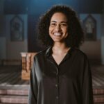 Portrait of a smiling woman with curly hair standing in a church setting with an altar.